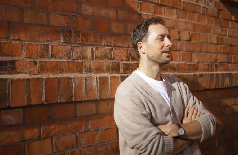 Simon Karim lehnt an einer Backsteinwand und spricht