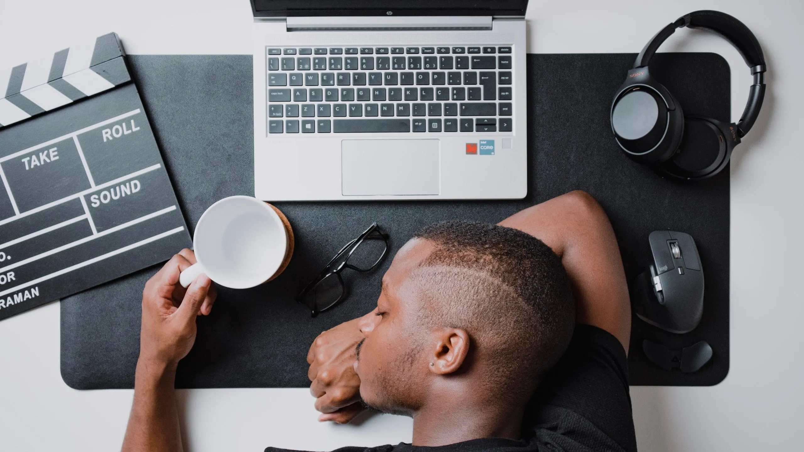 Ein Mann ist am Schreibtisch über seinem Laptop eingeschlafen, eine Tasse noch in der Hand