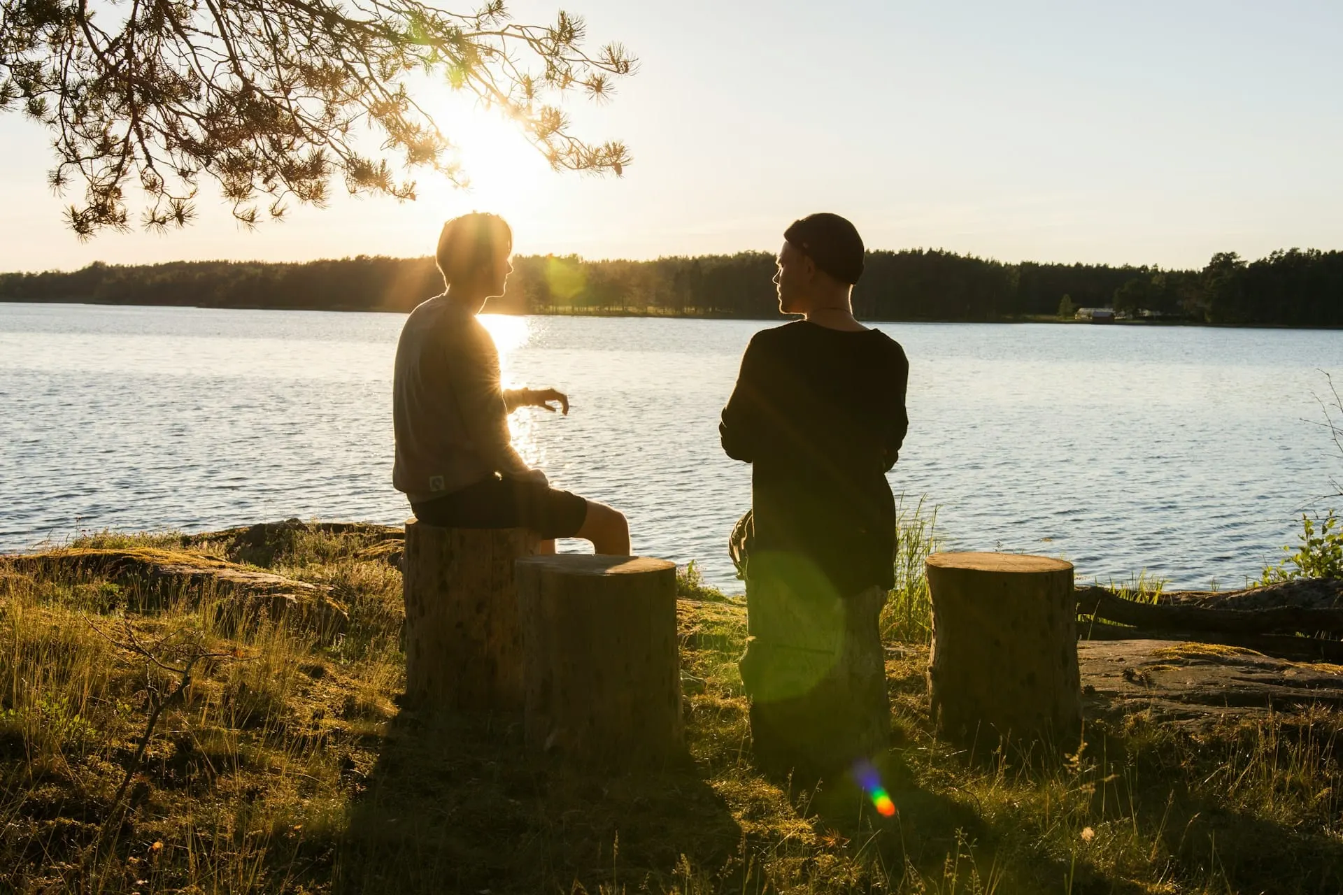 Zwei Männer sitzen im Abendlicht am See und sprechen miteinander