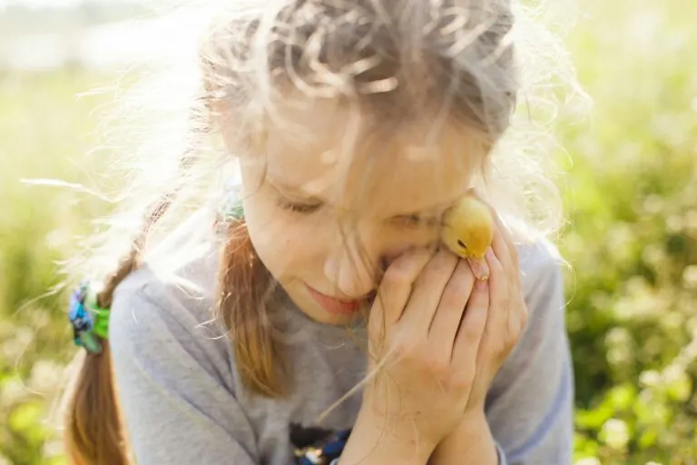 Mädchen mit geschlossenen Augen hält eine Blume an ihr Gesicht