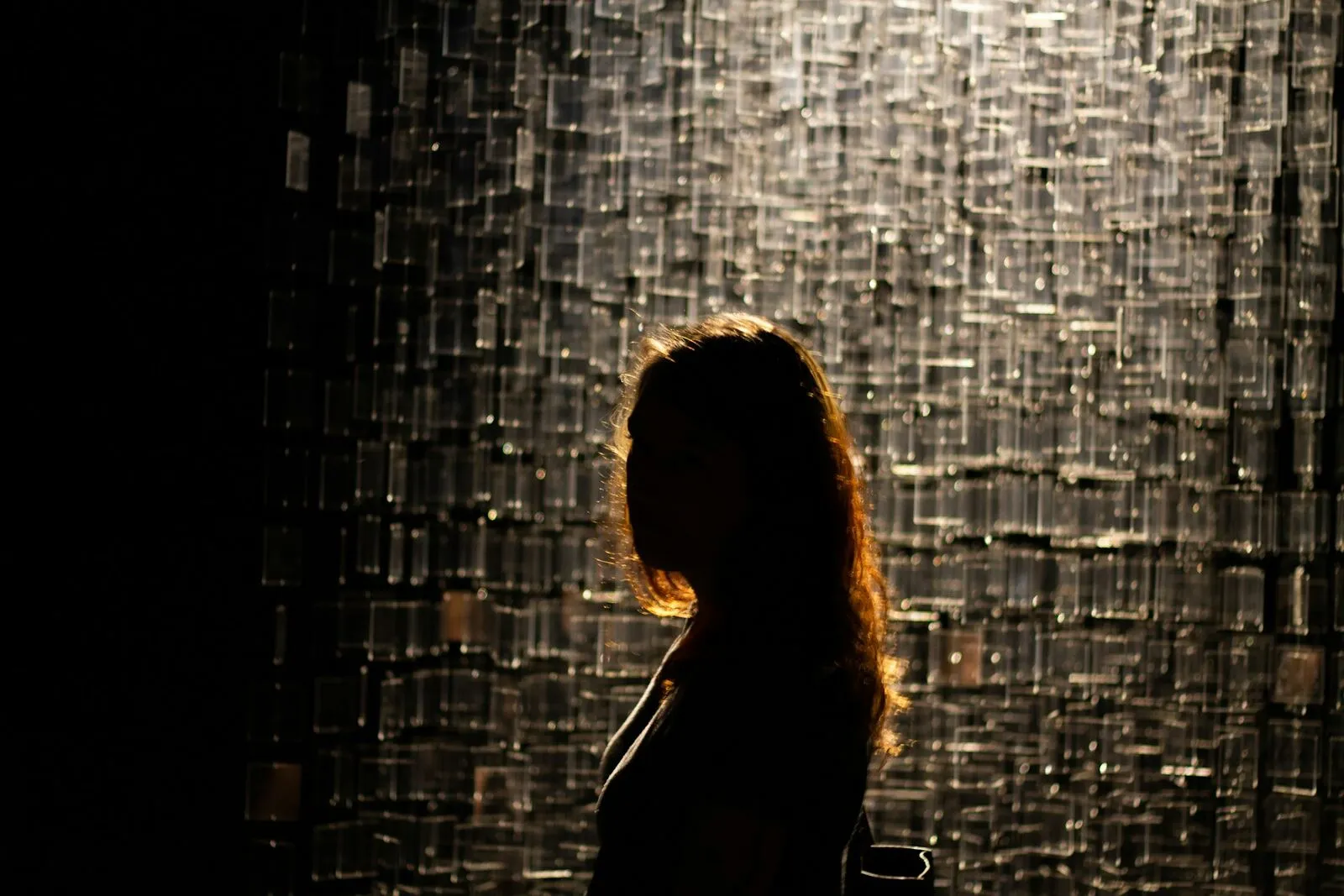 Silhouette einer Frau im Gegenlicht vor einer dunklen, schimmernden Wand