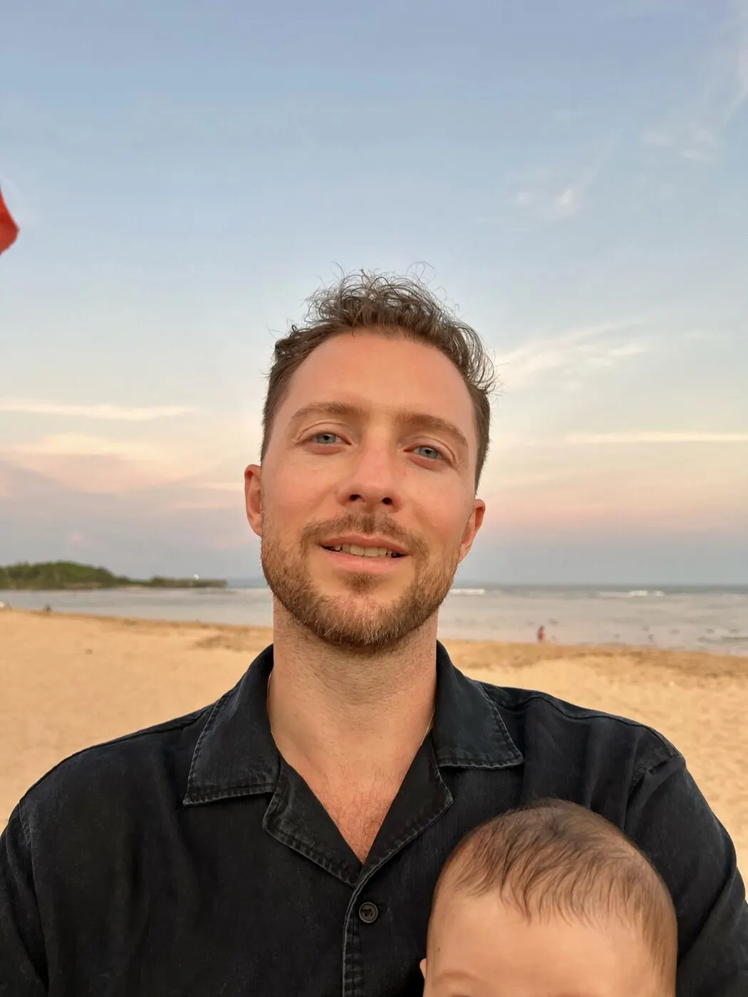 Simon Karim am Strand im Abendlicht, sein Kind im Arm