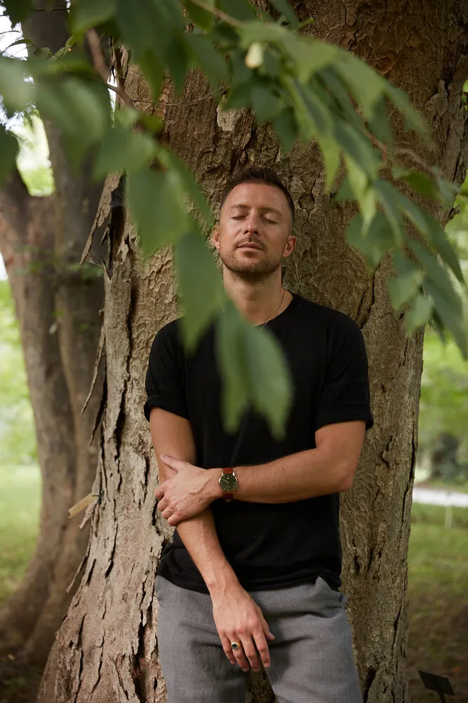 Simon Karim lehnt mit geschlossenen Augen an einem Baum