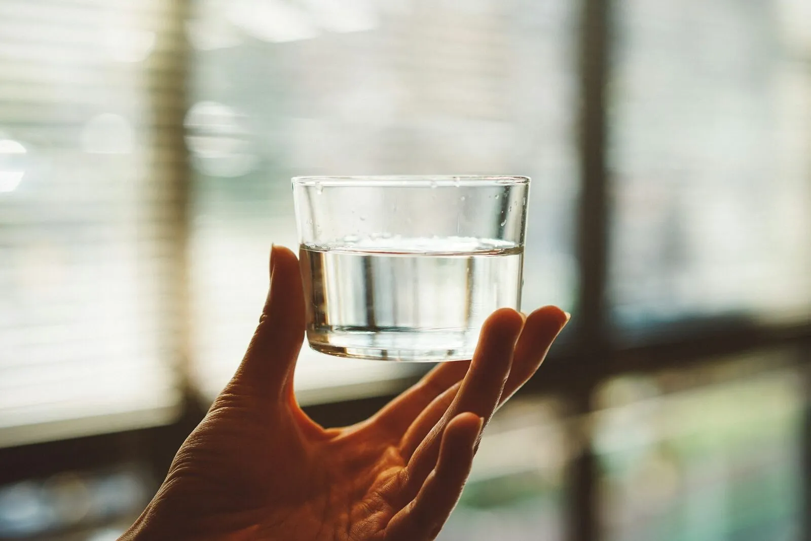 Eine offene Hand hält behutsam ein Glas mit stillem Wasser im weichen Tageslicht