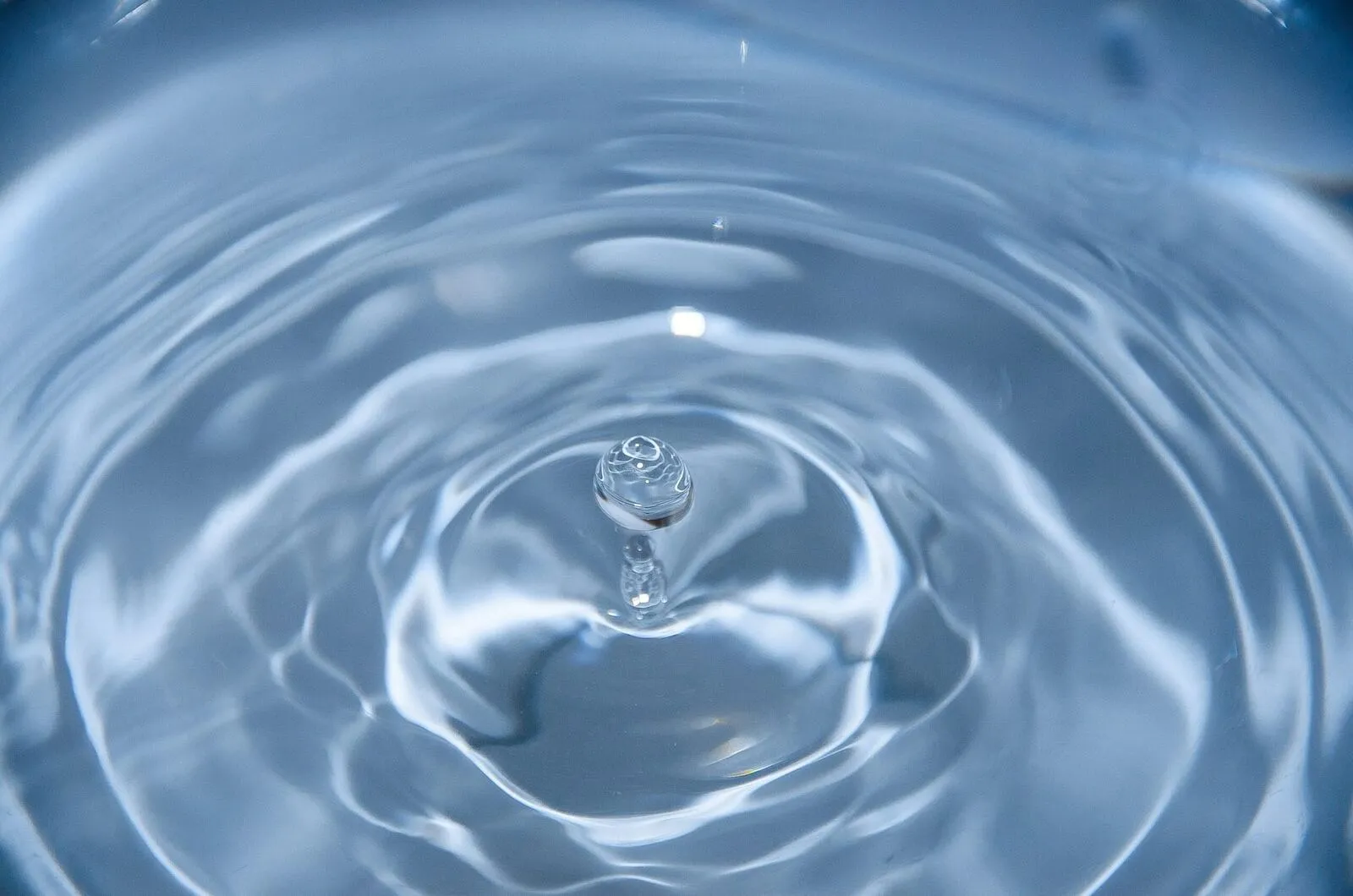 Ein einzelner Wassertropfen fällt in ruhiges Wasser und zieht feine kreisförmige Wellen
