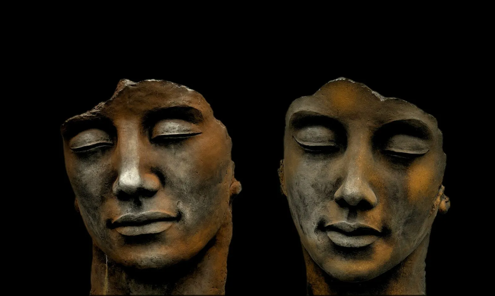 Zwei Skulpturen von Gesichtern mit geschlossenen Augen, nebeneinander mit respektvollem Abstand