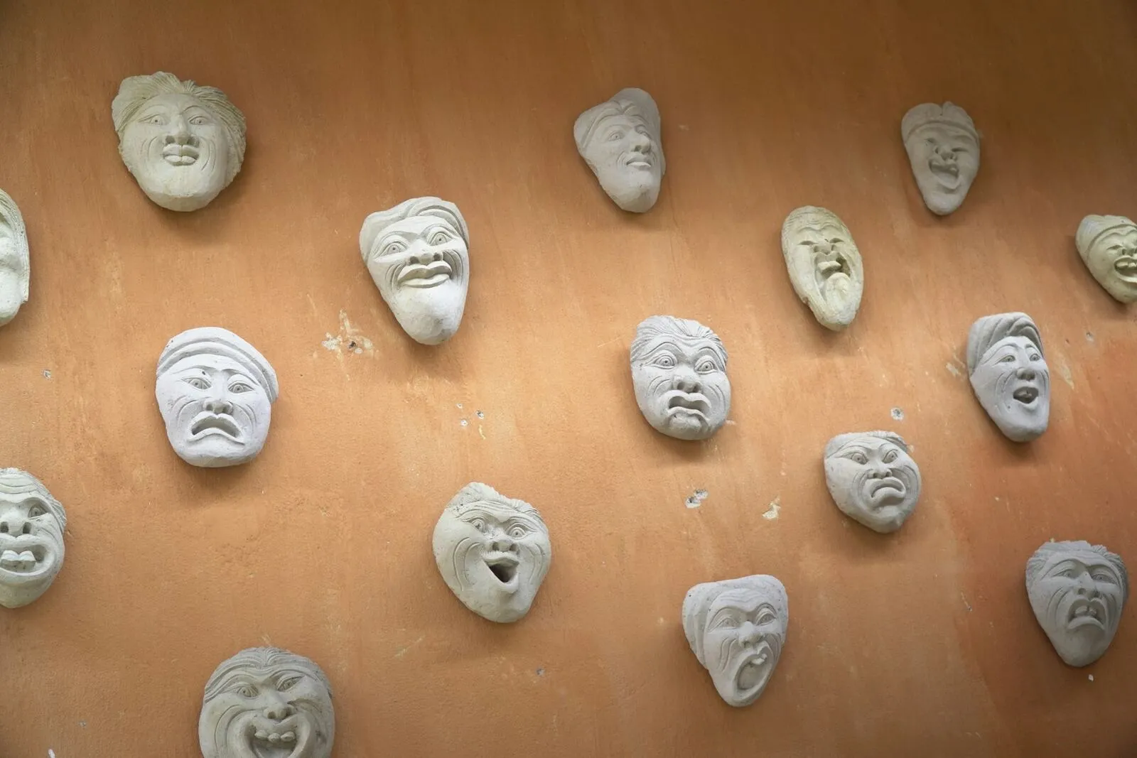 Viele kleine Gipsgesichter mit unterschiedlichen Gefühlsausdrücken an einer warmen Wand